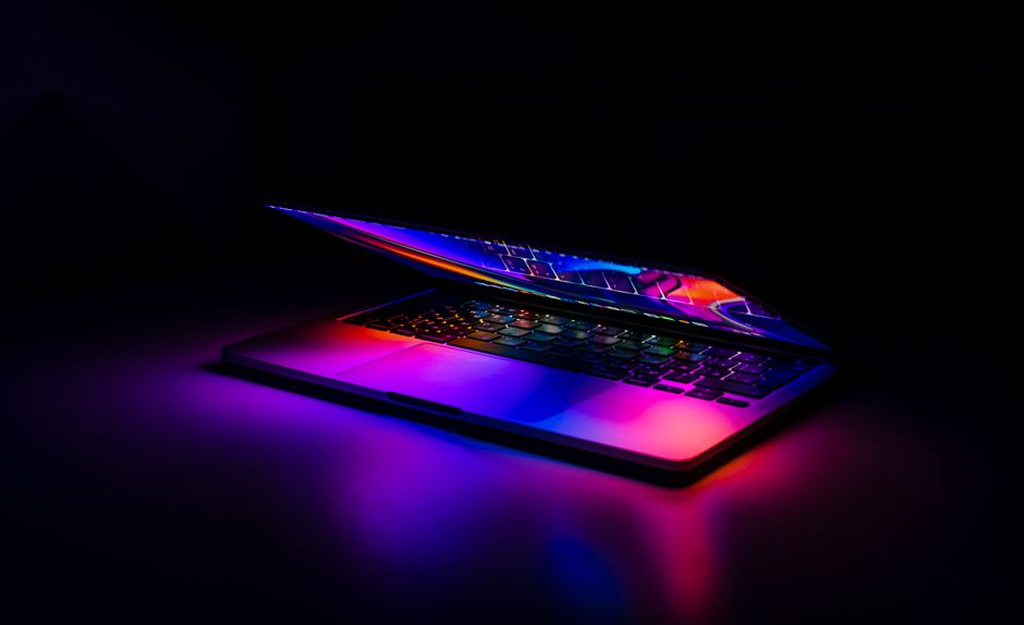 Djelomično zatvoreni MacBook s živim, šarenim odrazima svjetla na tamnoj podlozi.