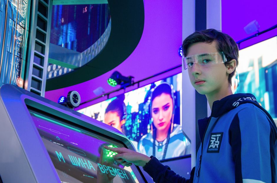 Teen boy in a digital room interacting with a futuristic touchscreen device wearing protective goggles.