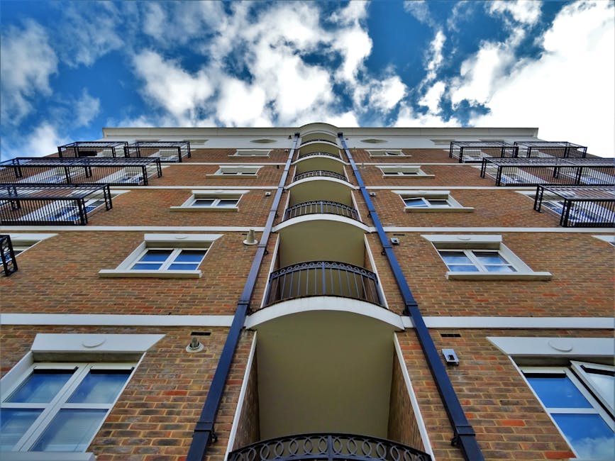 Low angle view of a modern urban apartment building with balconies under a clear blue sky.